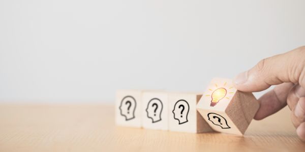Hand turning over a wooden cube from a head with a question mark in it to a lightbuib