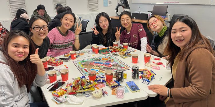 Students sitting round a table with sweets and drinks playing monopoly
