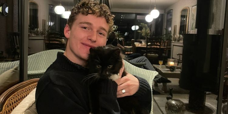 Young man sitting on chair cuddling a black cat with white paws