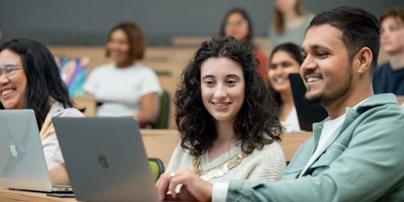 Two students looking at a laptop together in a lecture theatre.