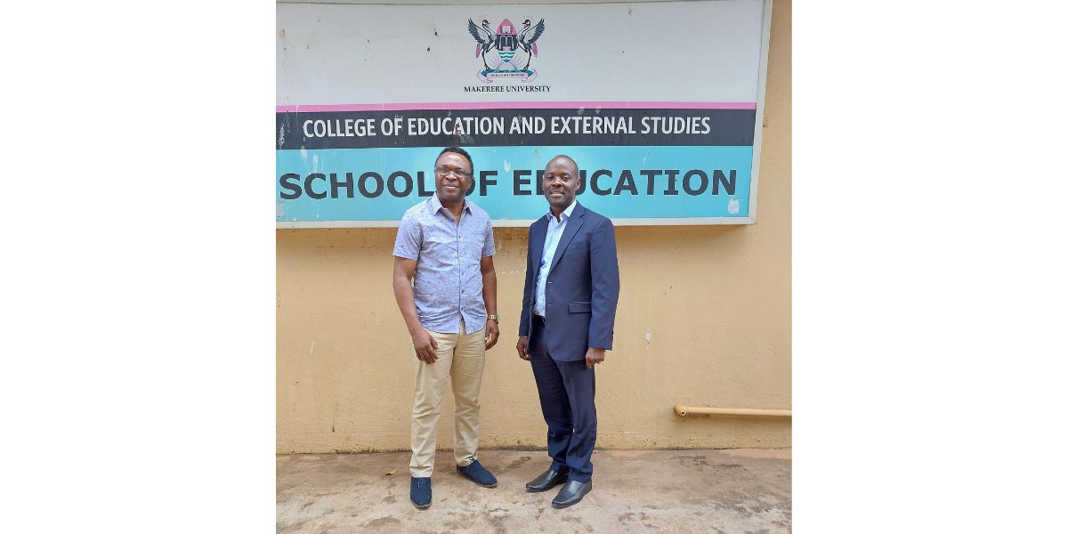 Two professors stood, smiling and shaking hands looking to camera in front of a School of Education sign outside.