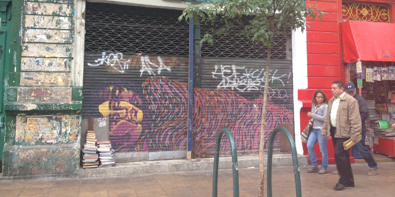 A man and a woman walking down the street in front of shutters covered in graffiti