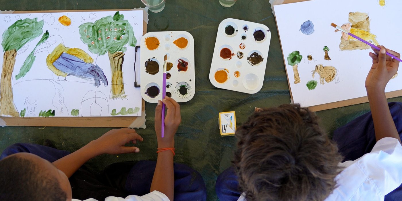 Two boys sitting on the ground, painting pictures