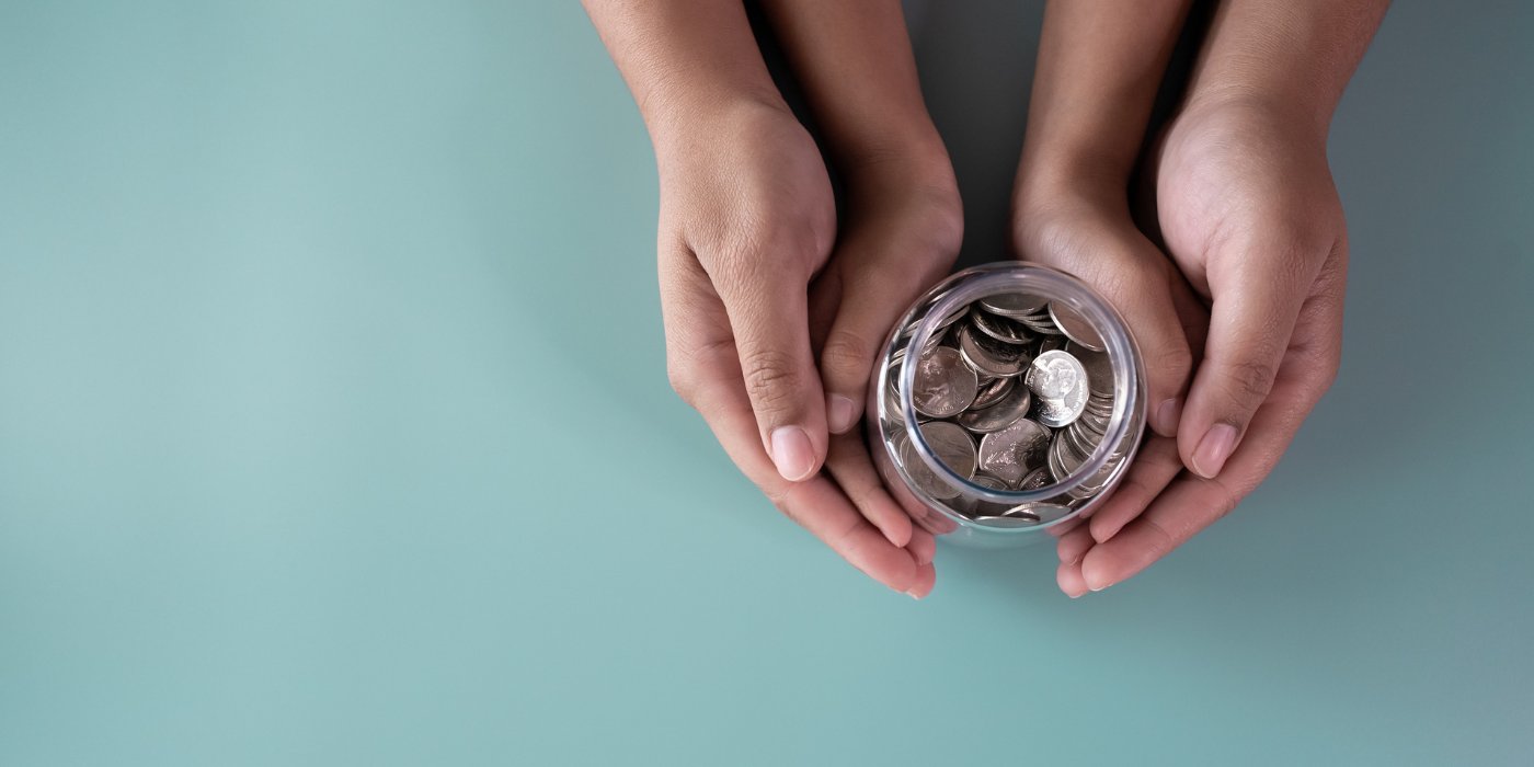 Two hands cupping a glass jar full of coins