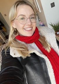 Selfie by Georgina, wearing red scarf and glasses and smiling at the camera.