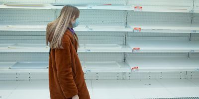 Woman in mask walking past empty shelves in a supermarket.