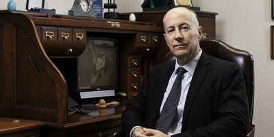 Picture of a man sat in a brown leather chair next to a brown wooden desk