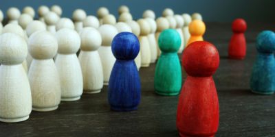 The image shows several wooden peg figures grouped together, with most of them being plain or natural-colored. In front of this group, there are a few brightly coloured peg figures in red, blue, green, and orange.