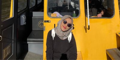 Alumna Farisca Utami stands in front of a yellow water taxi, she's smiling.