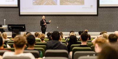 Presenter stood speaking to a seated audience in a lecture theatre