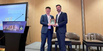 : Shuaihao Mi, a PhD candidate at the University of Leeds’ School of Law, receiving the Silver Medal award from a presenter at the International Insolvency Institute's conference in Singapore. Both are smiling and standing on a stage.