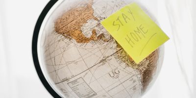 A globe with a Post-it note stuck onto it. The Post-it note reads: STAY HOME