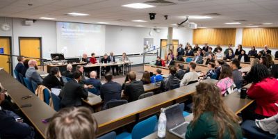 A crowded lecture hall, with the panel of speakers at the front.