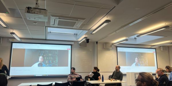 Dr Claudia Coveney is introduced by Dr Miro Griffiths at her book launch event. She is seated at a table with Dr Tom Campbell and Emeritus Professor Mark Priestley.