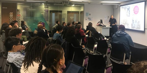 Photograph taken from back of the SSP seminar rooms, showing 25+ people sitting across 3 rows all watching Dr Adam Elliott-Cooper who is visible presenting at the front of the room.