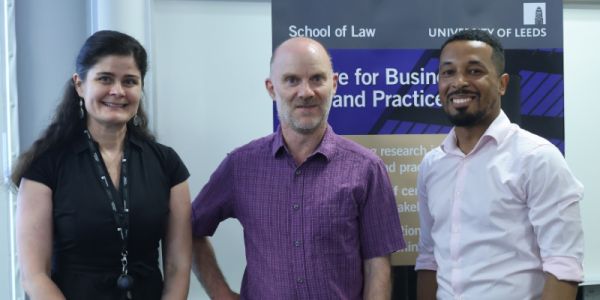Virag Blazsek, Duncan Sheehan and Sebastian Ricketts smile together next to a CBLP floor banner.