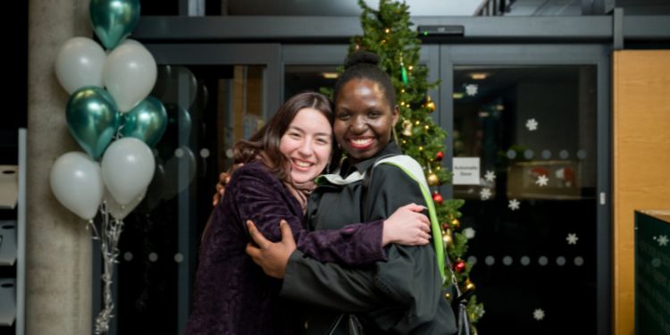 a grad and guest smiling and hugging.