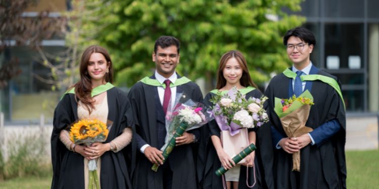 Four graduates holding flowers and degree certificates 