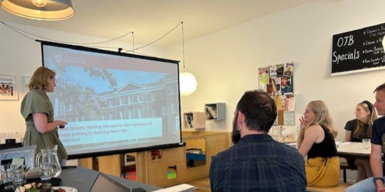 People watching a person presenting at the front of a cafe room. 