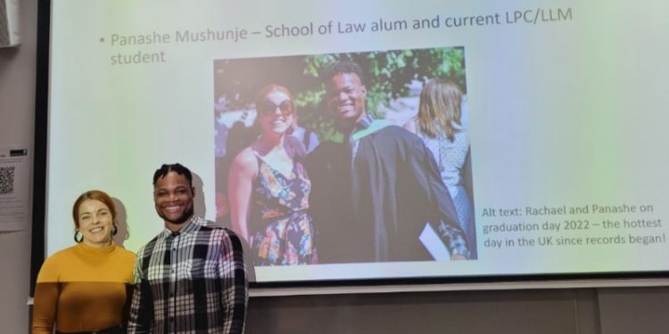Rachael and Panashe smile at the camera in front of a photo of them from graduation 