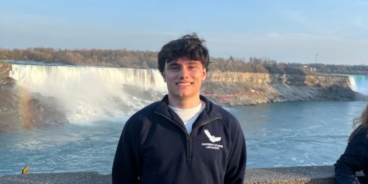 Student Louis Hempsall stands in front of the Niagara Falls, he is smiling