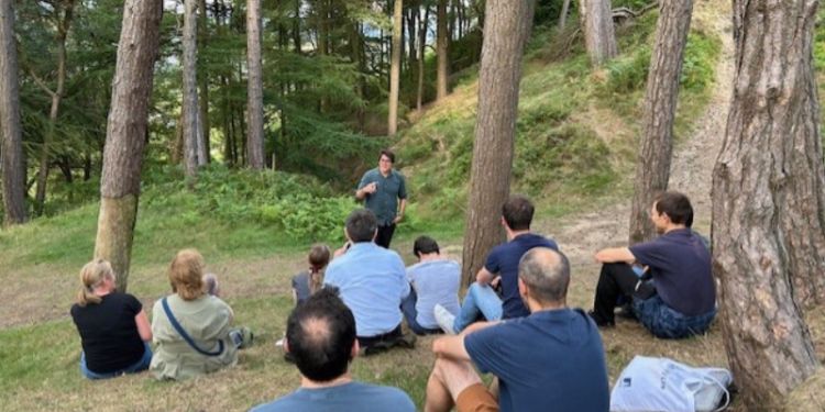 Participants sit in a woodland setting watching someone speak at the front. 