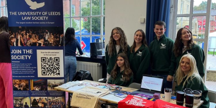 Members of the Law Society wearing green branded hoodies sitting and standing around a table at the Freshers Fair. 