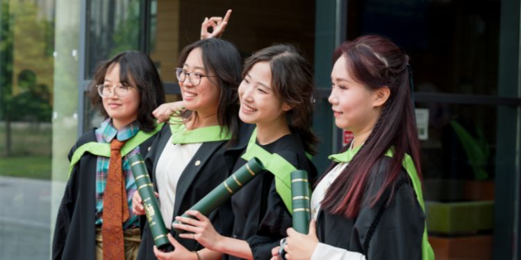 Four female graduates in gowns outside the building taken from the side