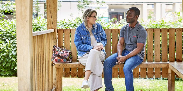 Two students sat talking on a bench on campus