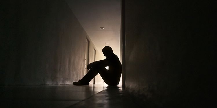 Man sitting in shadowy corridor looking dejected. 