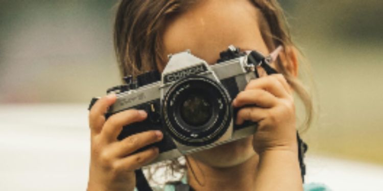 A child holds a camera in front of their face to take a photo.