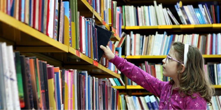 Child reaching up to take a book down from the library shelf