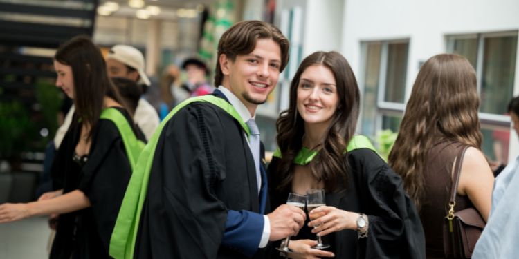 Two graduates in gowns holding glasses of champagne