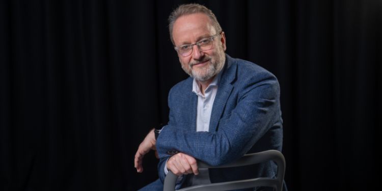 Richard Moorhead sitting on a chair in front of a black background.