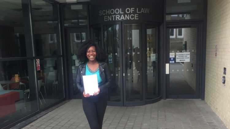 Oluwabunmi Adaramola standing outside the School of Law in June 2018, holding her third Year Dissertation.