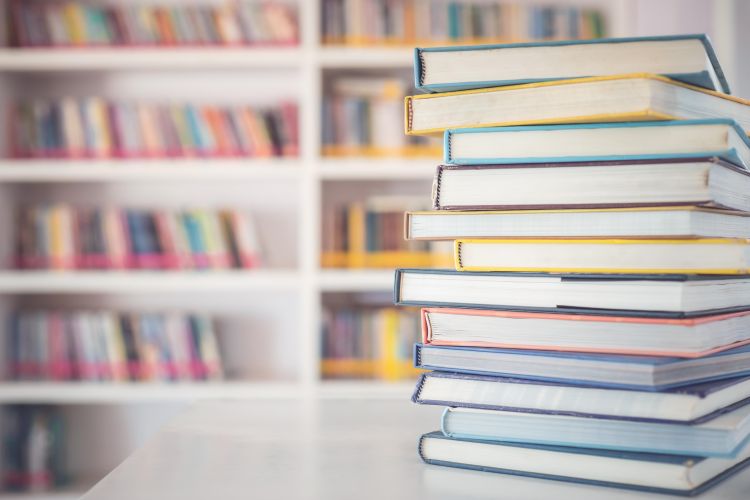 A stack of books on a table with a bookshelf shown in the background