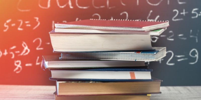 A pile of textbooks against a blackboard