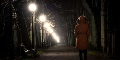 Lone person walking through a tree-lined path in a park at night.