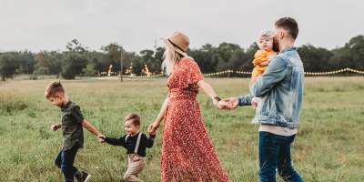 A family walking across a field: two young boys, a mum, and a dad carrying a baby