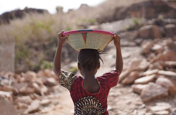 Young girl carrying basket on head over rough terrain