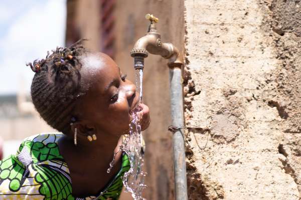 Young girl drinking from outdoor water tap in Africa